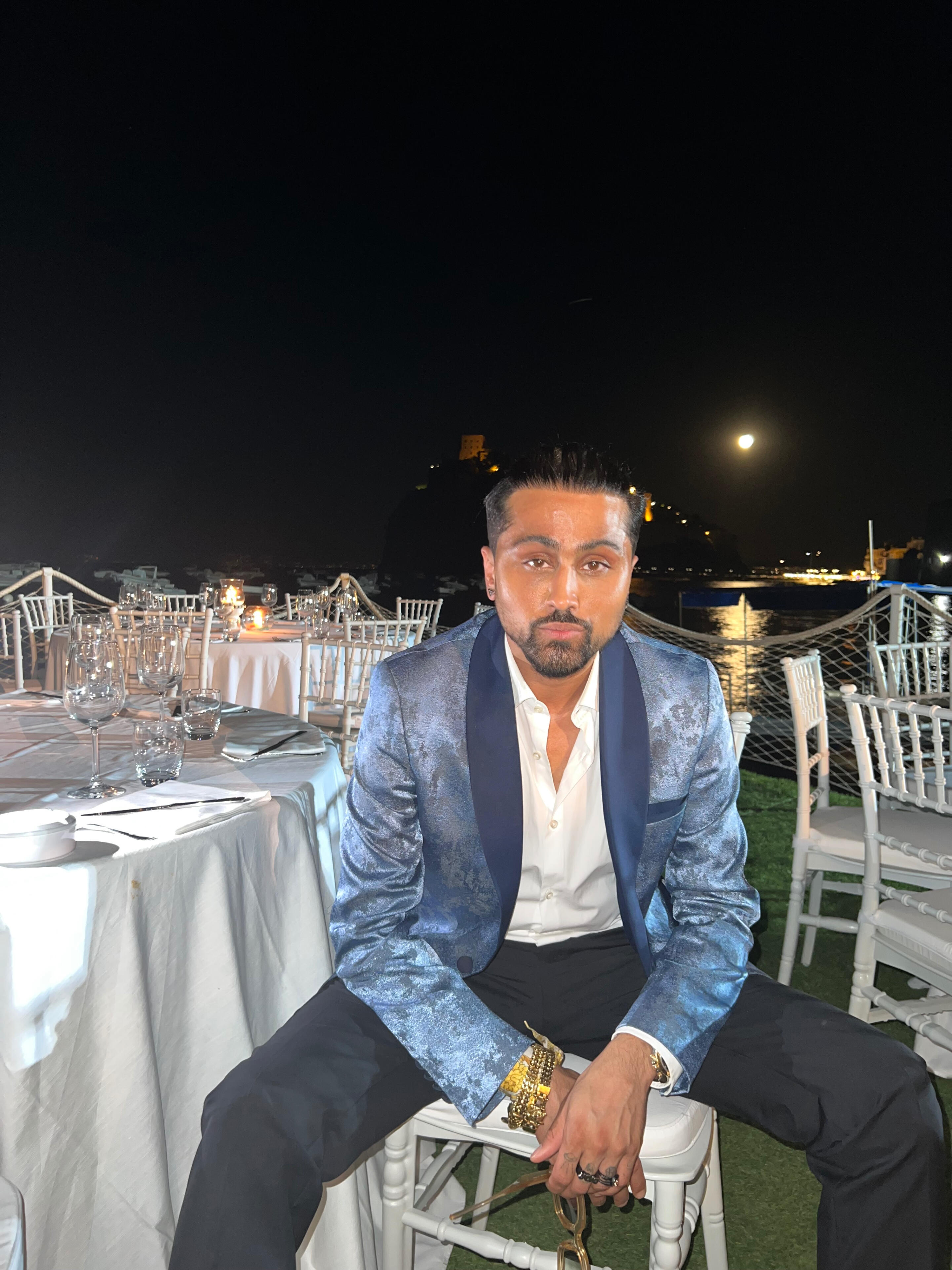 Samuel Sohebi — Ischia Global Film & Music Festival, private moment following the Ischia People Award (2022), reflecting his pre Samuel Sohebi seated at an evening event during the Ischia Global Film & Music Festival, photographed after receiving the Ischia People Award 2022, wearing a tailored evening look by the waterfront setting.