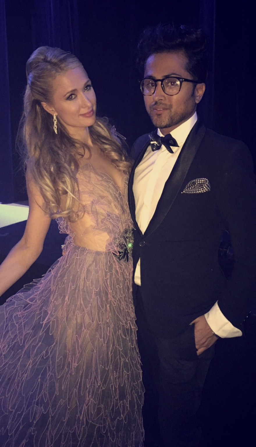 Paris Hilton in der graurosafarbenen Robe von Janina Couture neben Samuel Sohebi, der einen dunklen Smoking, eine Fliege und eine Brille trägt, 2015.