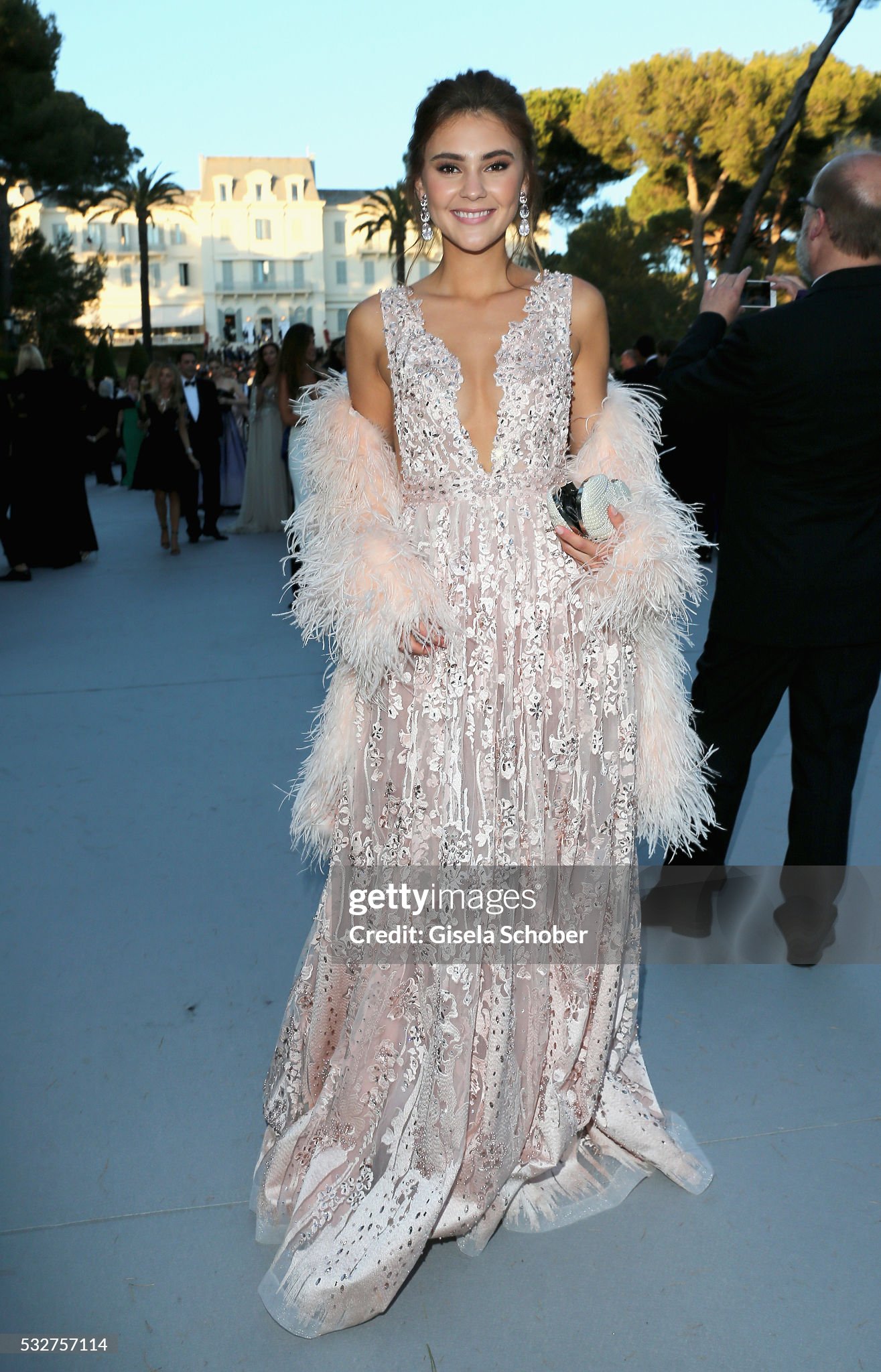 Stefanie Giesinger in einer bodenlangen roséfarbenen Robe mit floralen Verzierungen, tiefem V-Ausschnitt und Federstola vor dem Hôtel du Cap-Eden-Roc.