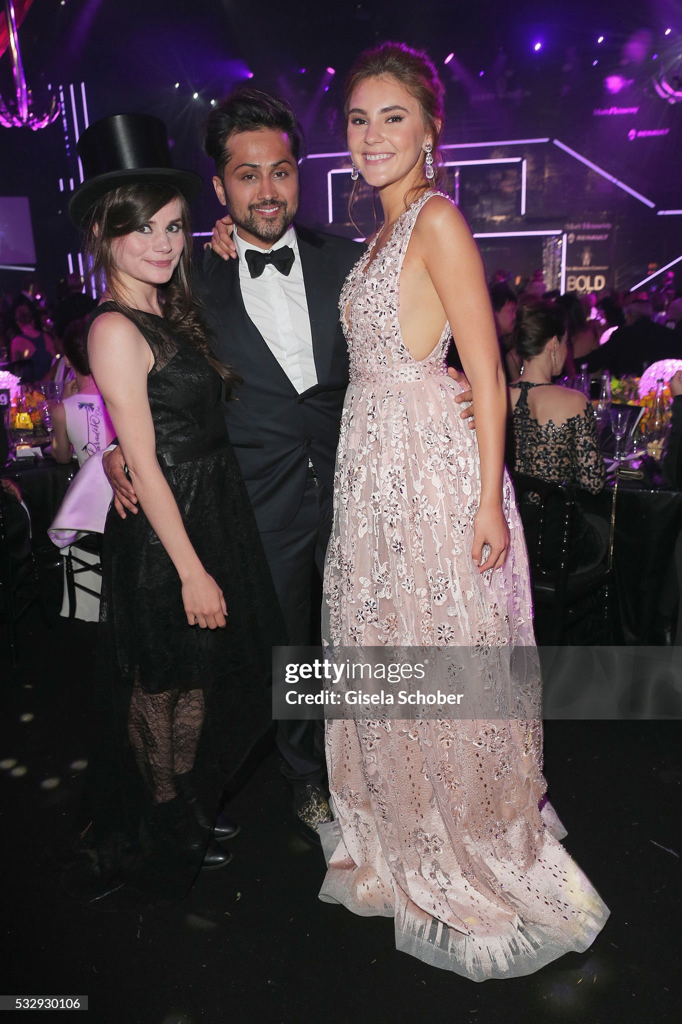 Stefanie Giesinger in einer roséfarbenen Abendrobe neben Samuel Sohebi im Smoking und einer weiteren Gästin im schwarzen Kleid mit Zylinder beim amfAR-Dinner 2016.