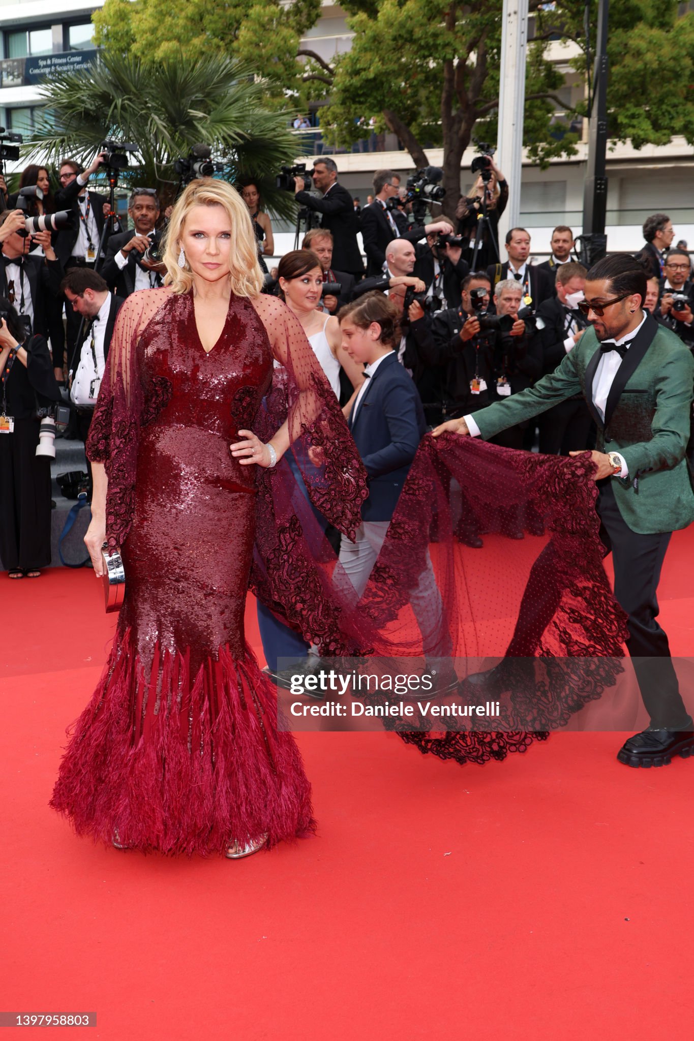 Veronica Ferres auf dem roten Teppich in Cannes in einer burgunderroten Paillettenrobe mit transparenter Spitzencape-Schleppe; Samuel Sohebi arrangiert die Schleppe.
